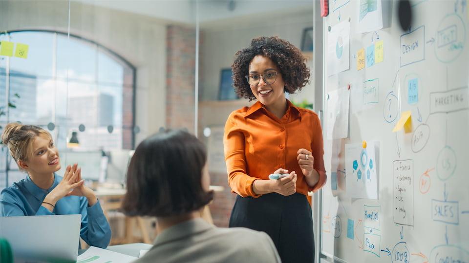 A woman standing at a whiteboard and talking with colleagues